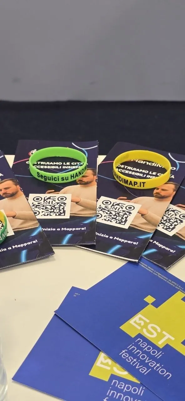 Cartoline di HandiMap con codice QR e braccialetti verdi «Seguici su HandiMap», accanto ai pieghevoli di EST