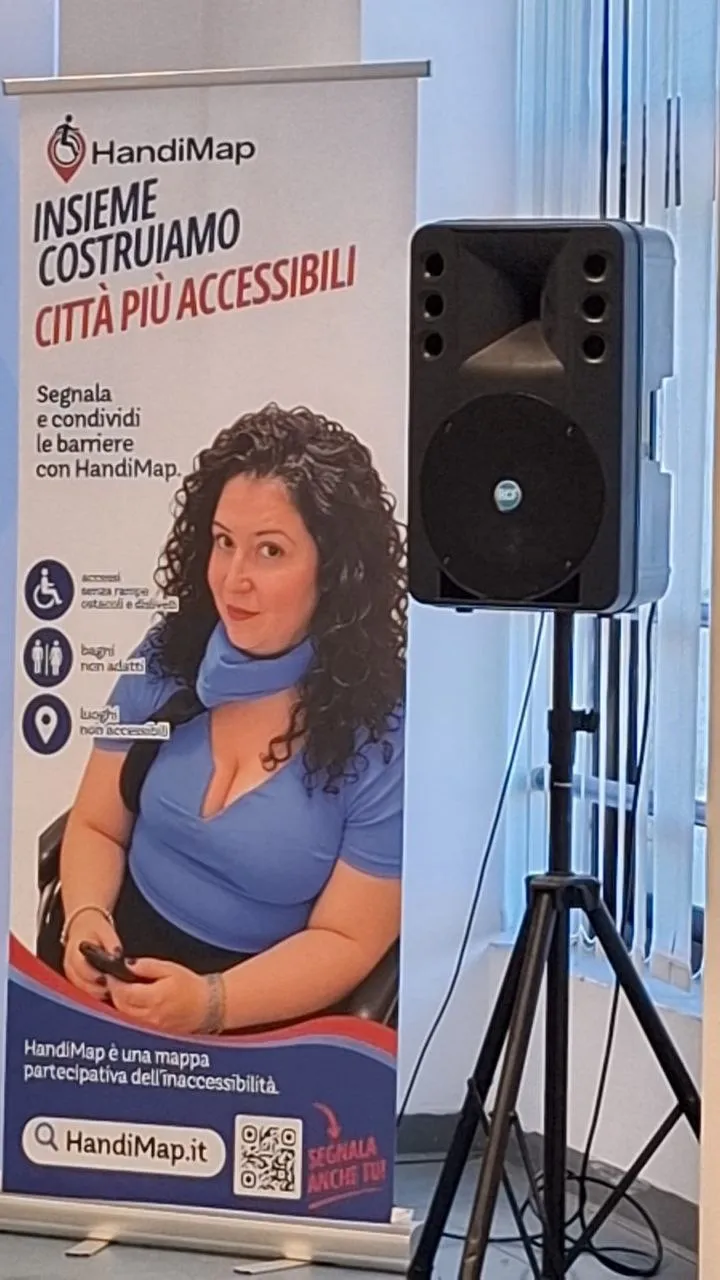 Roll-up di HandiMap «Insieme costruiamo città più accessibili» con la foto di Manilla, accanto a una cassa audio