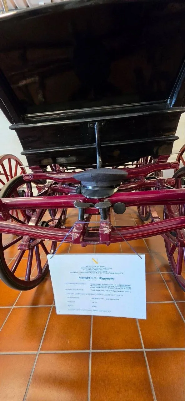 Particolare delle ruote rosse e della cassa nera di una carrozza, con il cartello descrittivo