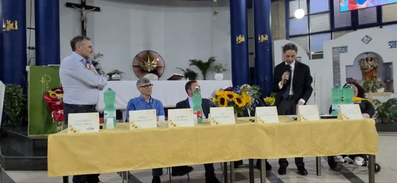 Un relatore al microfono accanto al tavolo addobbato con i girasoli