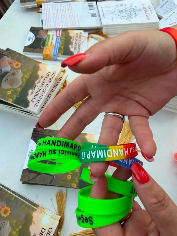 Braccialetti verdi di HandiMap tenuti in mano sopra le copie del libro