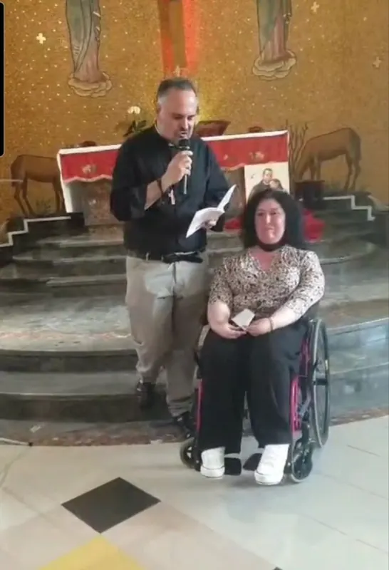 Manilla davanti all'altare della Chiesa del Sacro Cuore, accanto a un uomo che legge al microfono